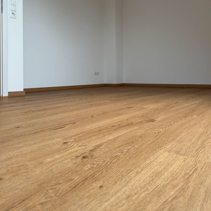 Fertig verlegter Klebevinylboden in Holzoptik mit weißer Tür und Sockelleisten – Projekt von bodenhero